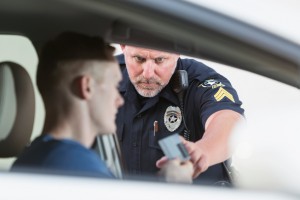 Serious police officer pulling over a young driver for a traffic violation. Focus on the policeman.